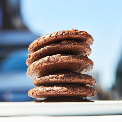 A stack of six chocolate fudge cookies with chocolate chunks on a surface.