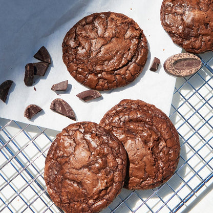 Rich double chocolate cookies with a glossy, crackled surface cooling on a wire rack, surrounded by chunks of dark chocolate.