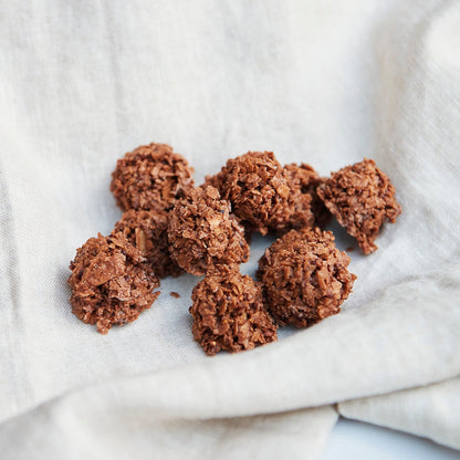 C by C New York Sobacha Crunch clusters made with roasted buckwheat and chocolate, arranged naturally on a soft beige linen cloth for a warm, artisanal look.