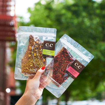 A hand holding two packages of branded toffee products with visible nuts and chocolate.