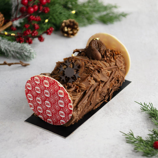 Chocolate yule log with a red and white base on a light background with Christmas decorations.