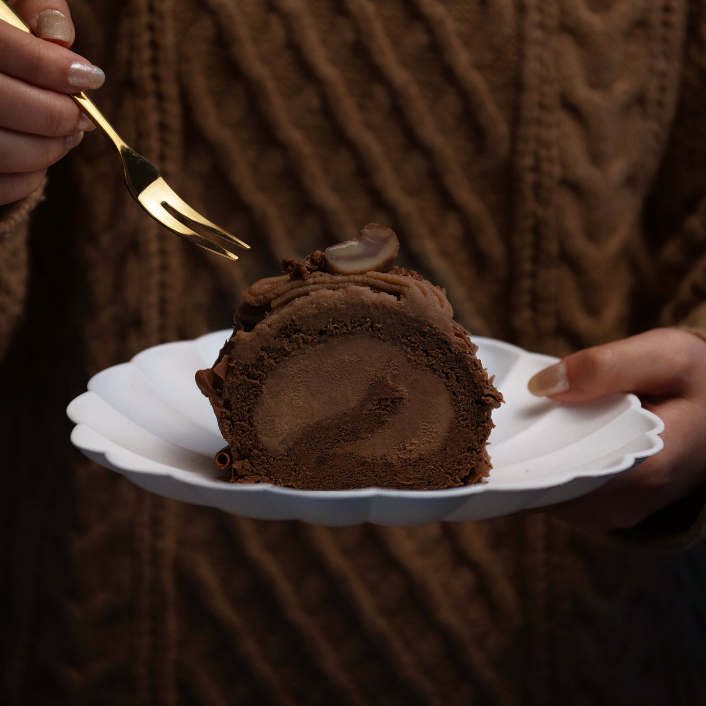 Chocolate dessert on a white plate held by a person wearing a brown sweater.