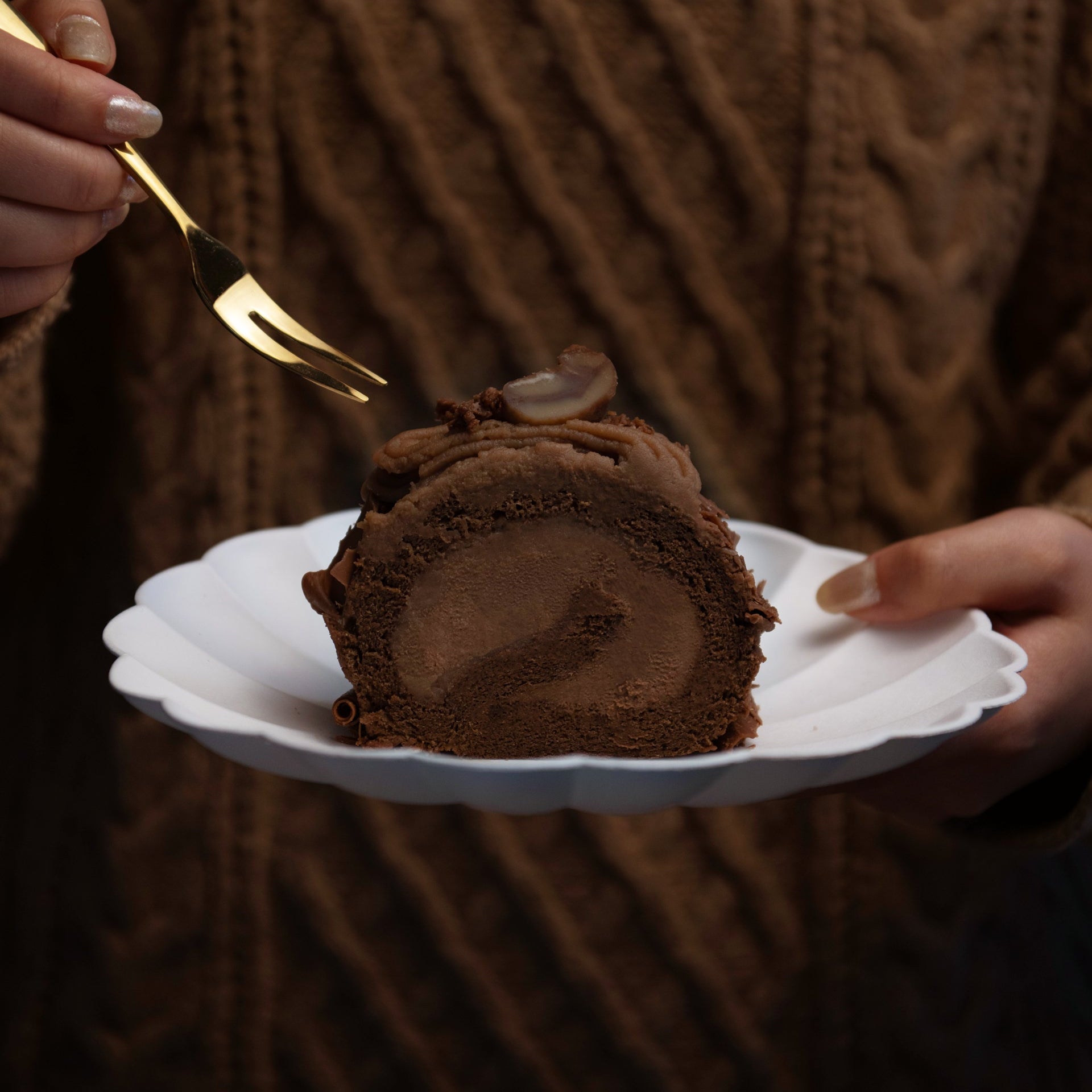 Chocolate dessert on a white plate held by a person wearing a brown sweater.