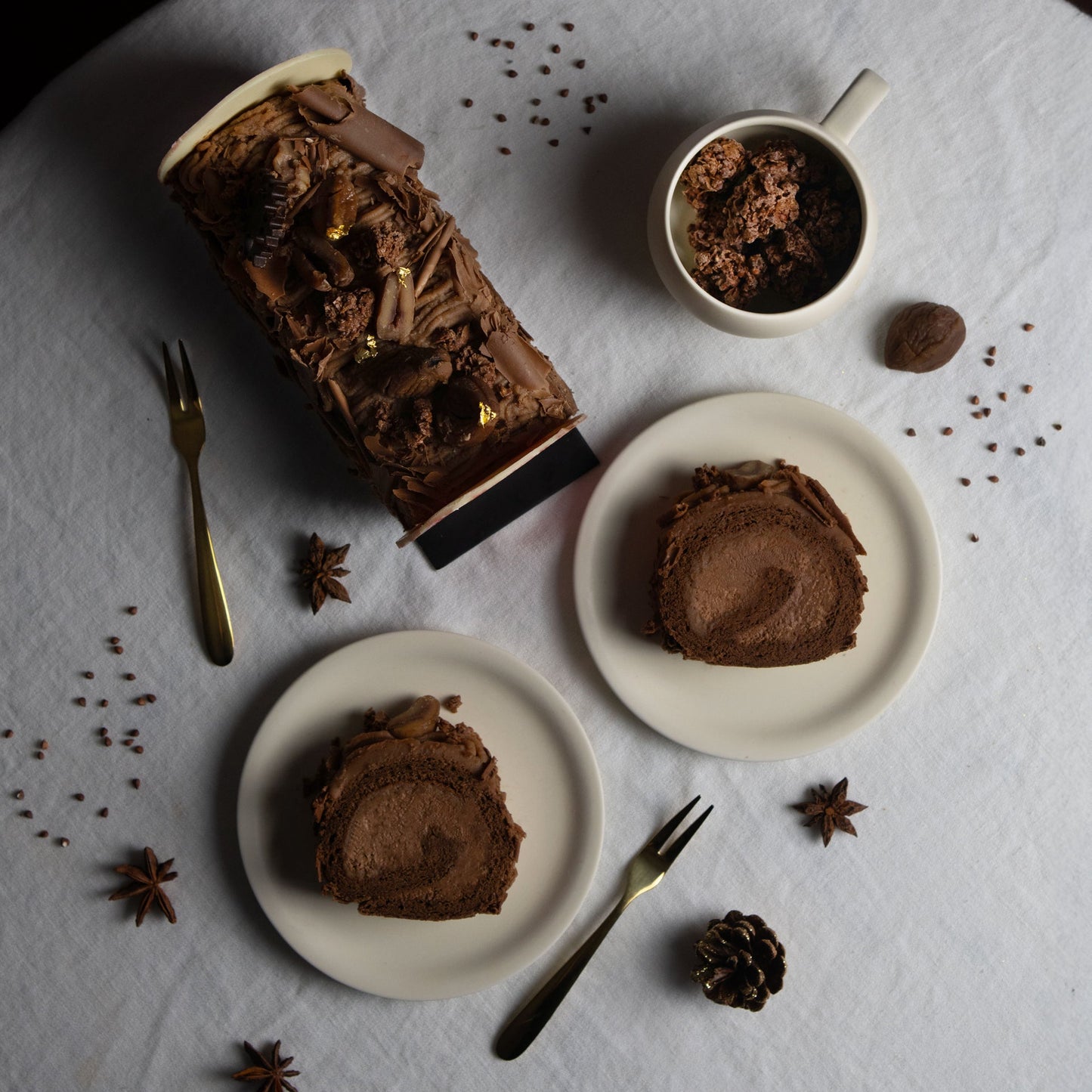Chocolate cake with slices on plates, a cup of coffee, and star anise on a white surface.