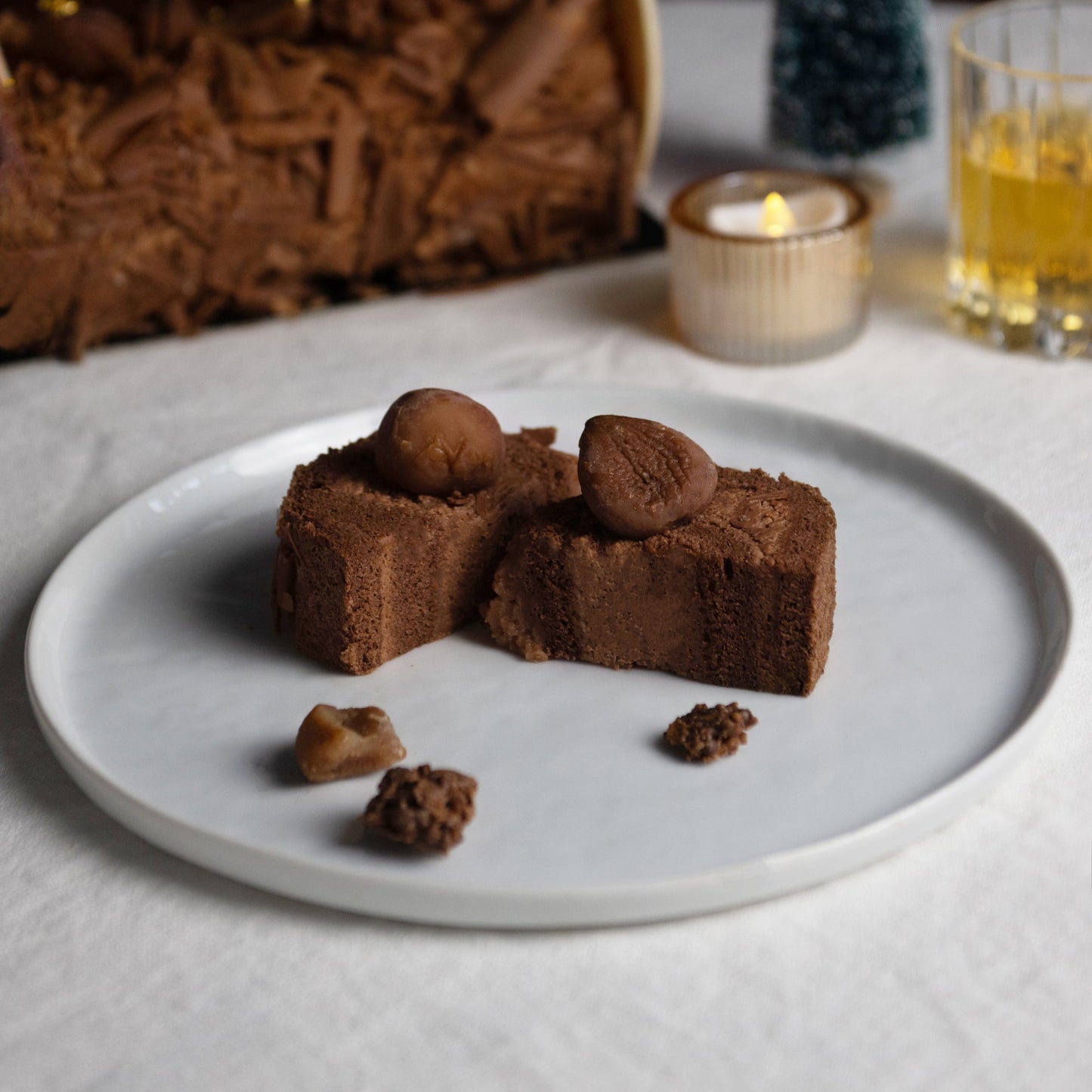 Chocolate dessert on a white plate with a candle and Christmas tree decoration in the background.