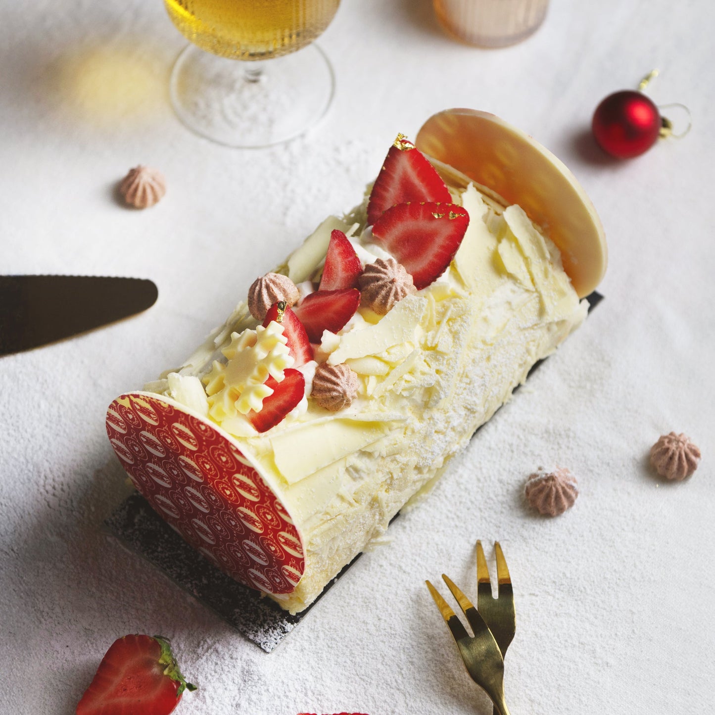 Yule log cake with strawberries and cream on a white surface with a glass of wine and candle.