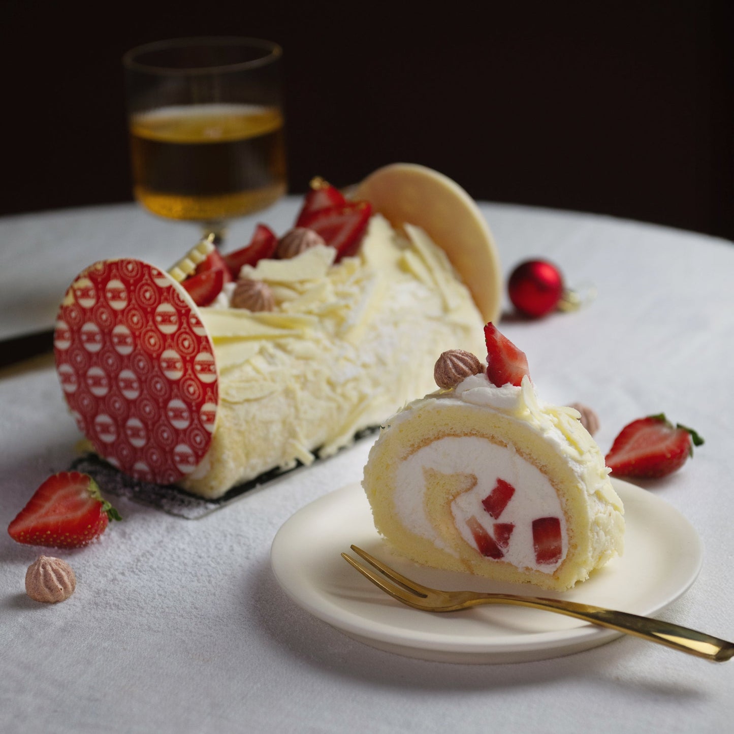 Sliced cake roll with strawberries on a white plate with a glass of beer in the background.