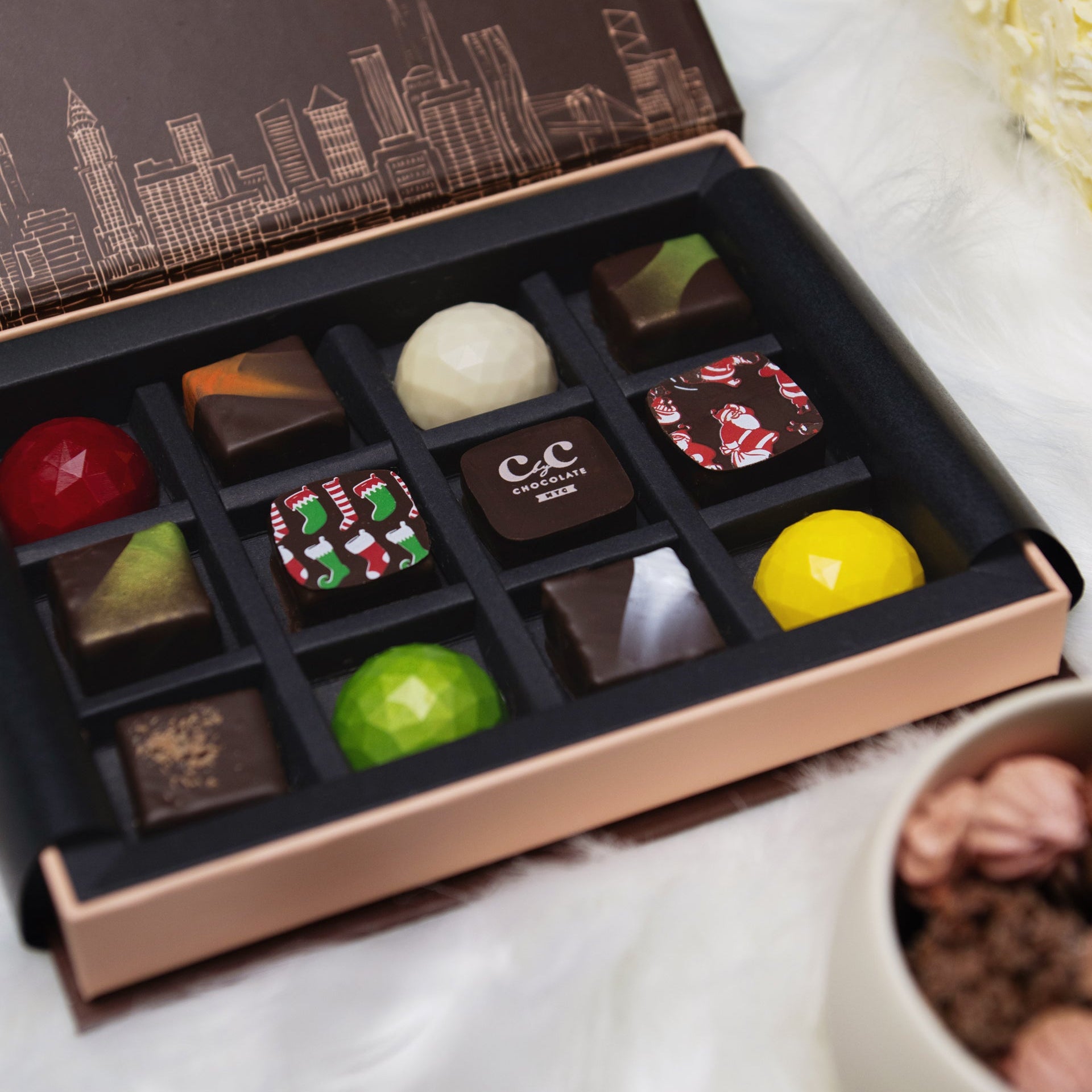 Open box of assorted chocolates with a cityscape design on the lid, placed on a white surface.