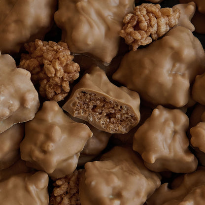 A close-up pile of chocolate-covered cereal clusters, with one piece broken open to show the textured rice cereal interior.